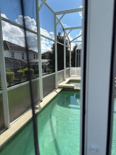 Screened lanai pool area with teal water and white frame enclosure overlooking residential neighborhood