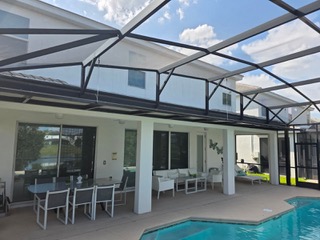 Modern patio with glass roof panels, white columns, dining table, chairs, and pool edge visible