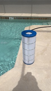 Pool filter cartridge standing on concrete deck next to swimming pool