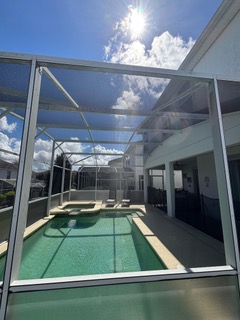 Screened-in pool area with clear glass panels and green deck under blue sky