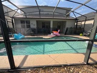 Screened-in residential pool with turquoise water and lounge chairs under metal canopy roof