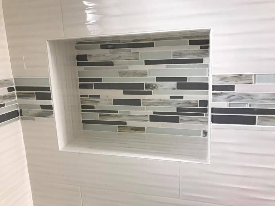 Bathroom tile display showing subway and linear mosaic tiles in white, gray, and black tones
