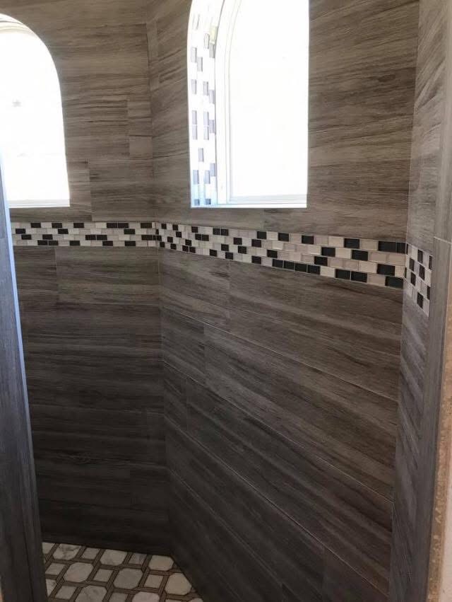 Modern shower enclosure with gray wood-grain tile walls and black and white mosaic accent band