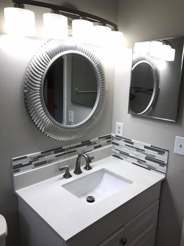 Modern bathroom vanity with white sink, bronze faucet, decorative textured mirrors, and lit sconces above tile backsplash
