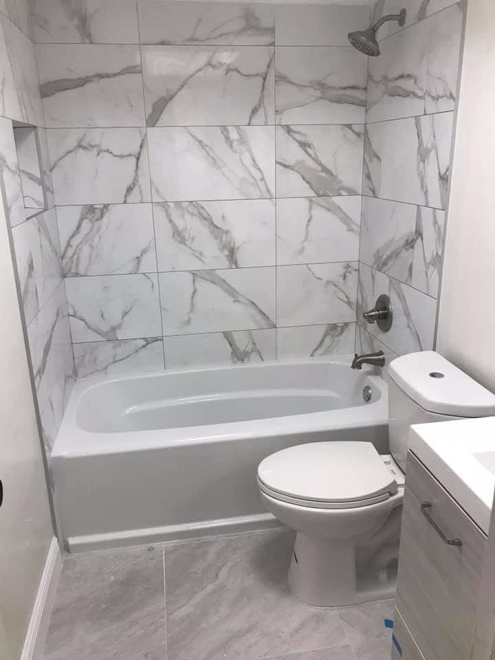 Modern bathroom with marble-look tile shower surround, white bathtub, toilet, and vanity