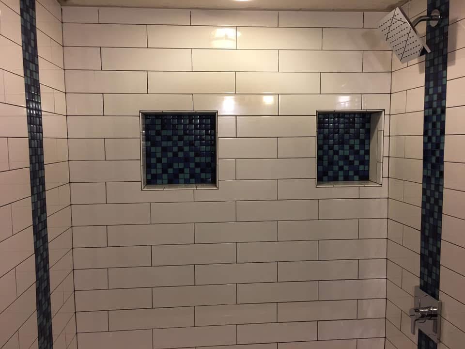 Modern bathroom shower with white subway tile walls, dark mosaic tile accents, and two inset shelving niches