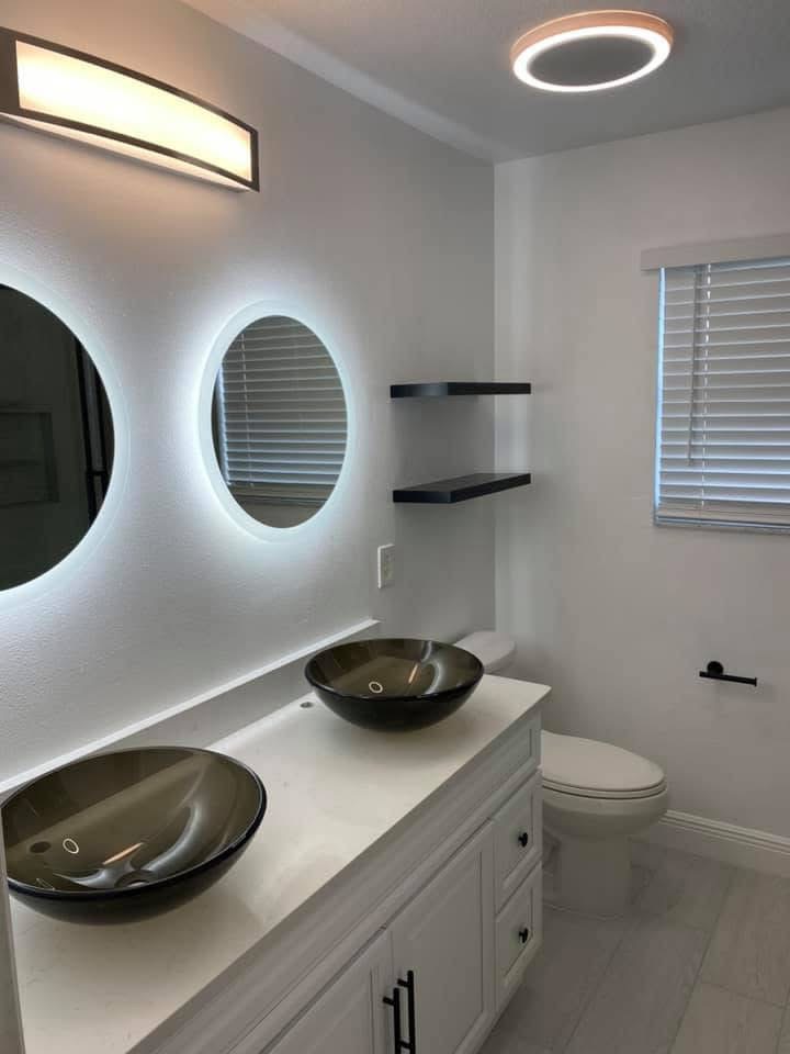 Modern bathroom with dual black vessel sinks, illuminated oval mirror, and white vanity