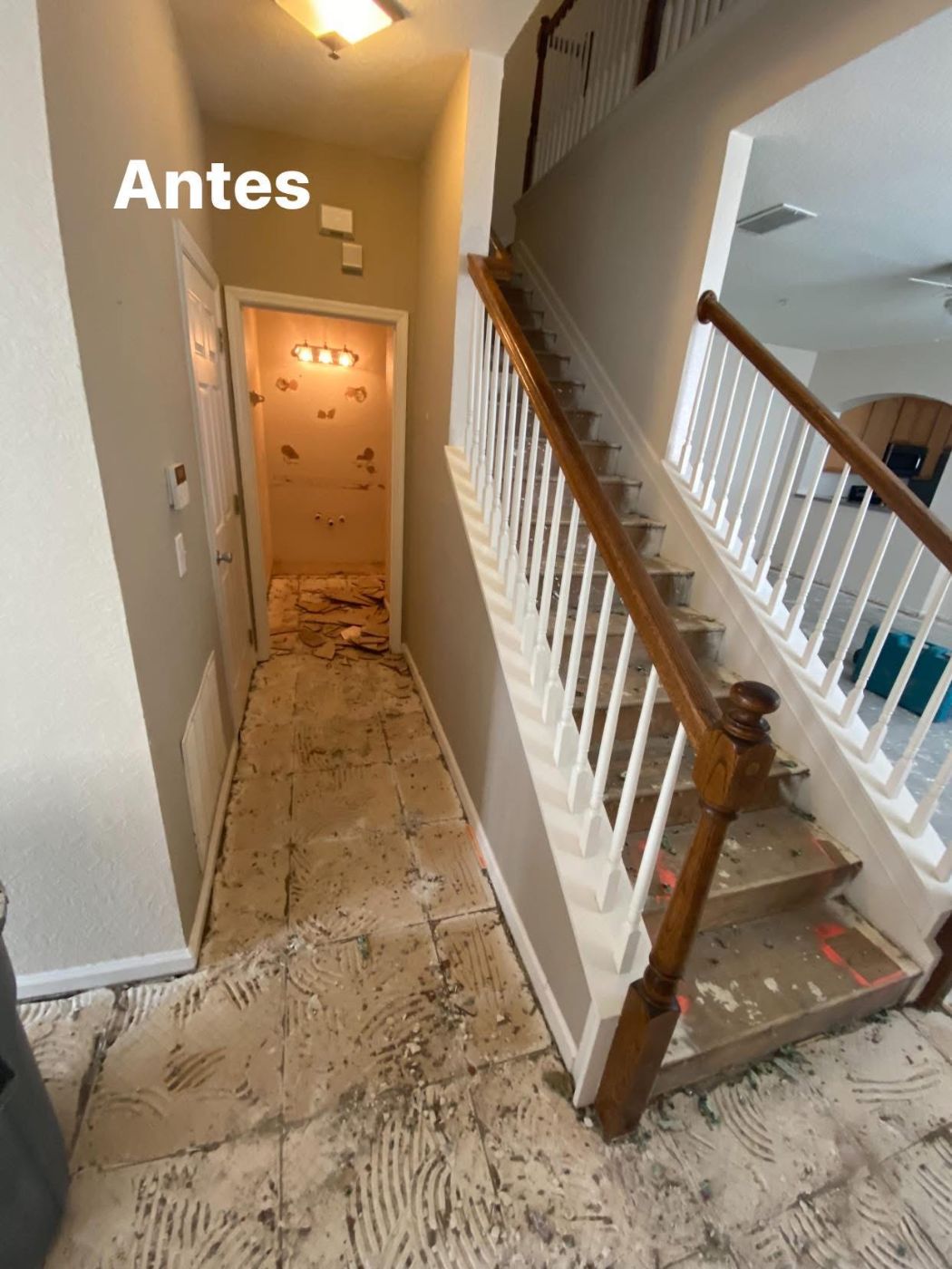 Hallway before renovation showing exposed subfloor, bare walls, and wooden staircase