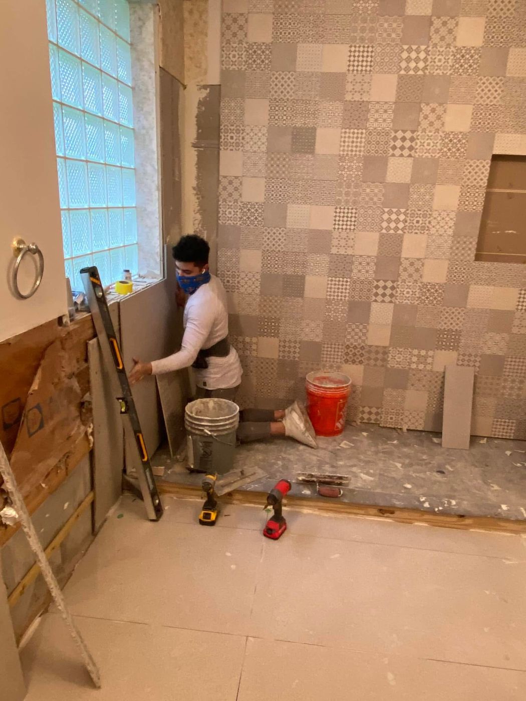 Worker in blue mask installing patterned tile wall in bathroom renovation