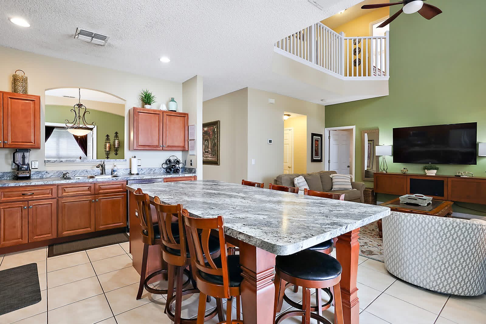 Open-concept kitchen and living room with marble island, wood cabinetry, and green accent wall