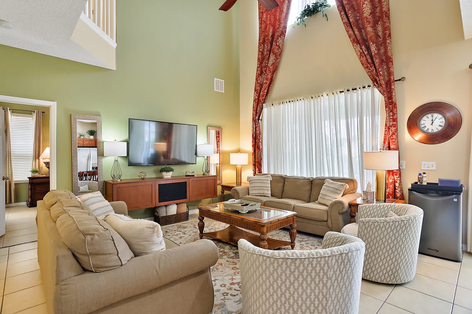 Spacious living room with beige seating, wood entertainment center, green accent walls, and high ceilings