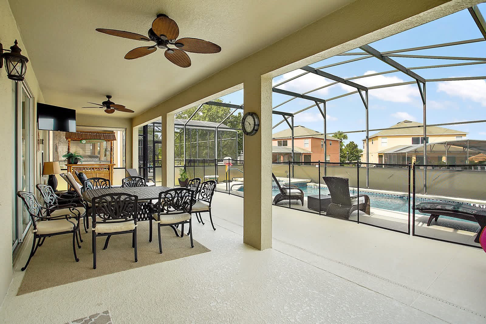 Screened lanai with ceiling fans, seating area, and view of pool and neighboring homes