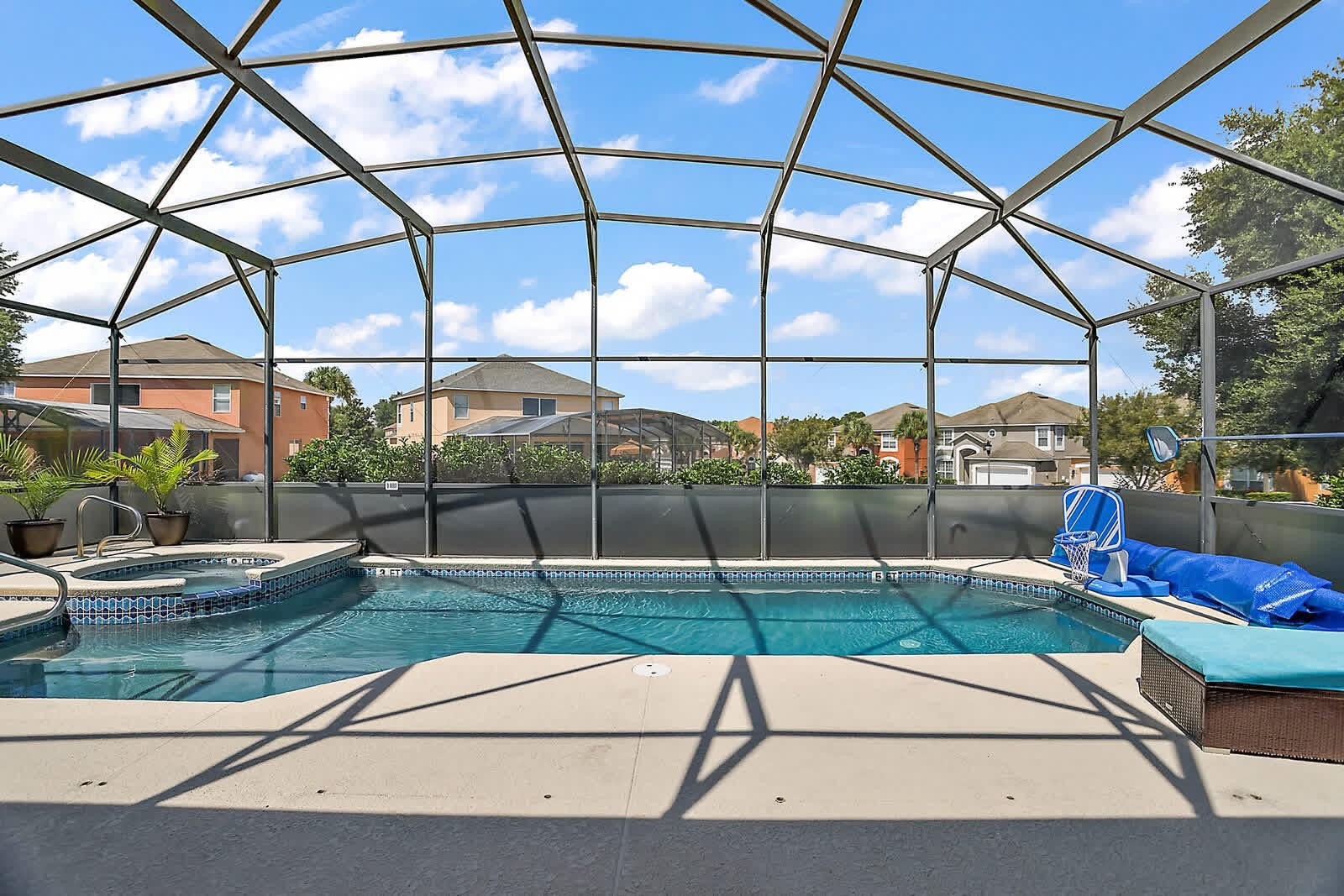 Screened-in residential pool with turquoise water, concrete deck, and neighborhood homes visible beyond