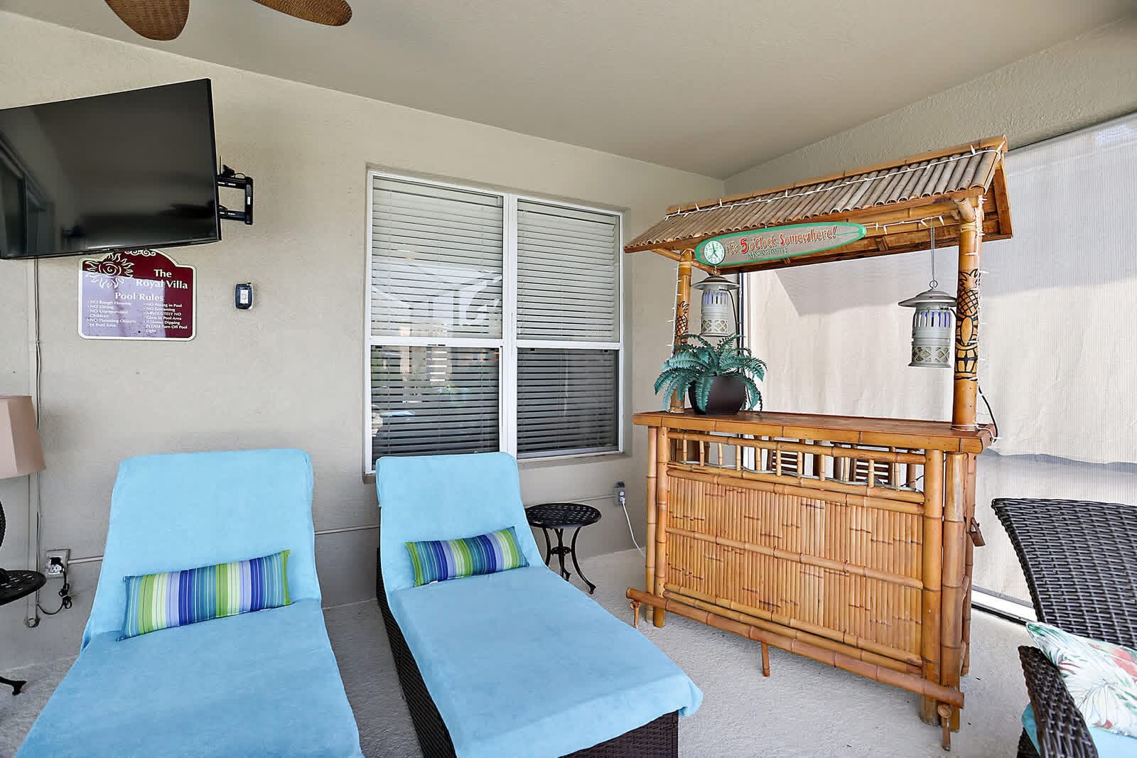 Pool house interior with two blue lounge chairs, wooden tiki bar, and wall-mounted TV