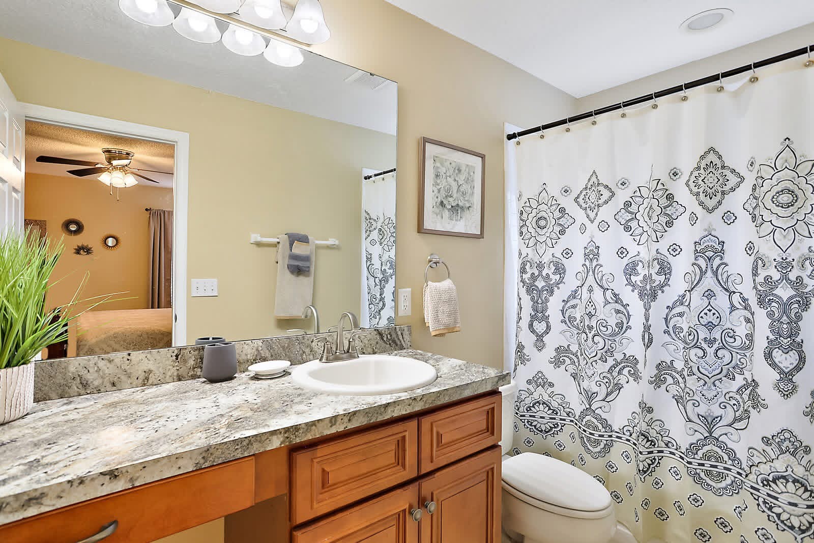 Modern bathroom with granite vanity, wooden cabinets, ornate shower curtain, and large mirror