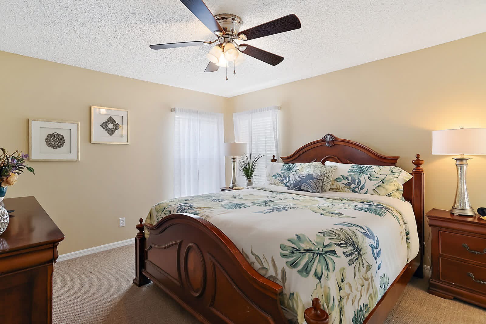 Spacious master bedroom with wood bed frame, ceiling fan, cream walls, and floral bedding