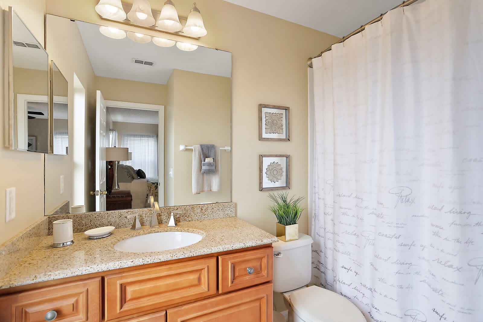 Bright bathroom with beige walls, granite countertop, wooden vanity, large mirror, and white shower curtain