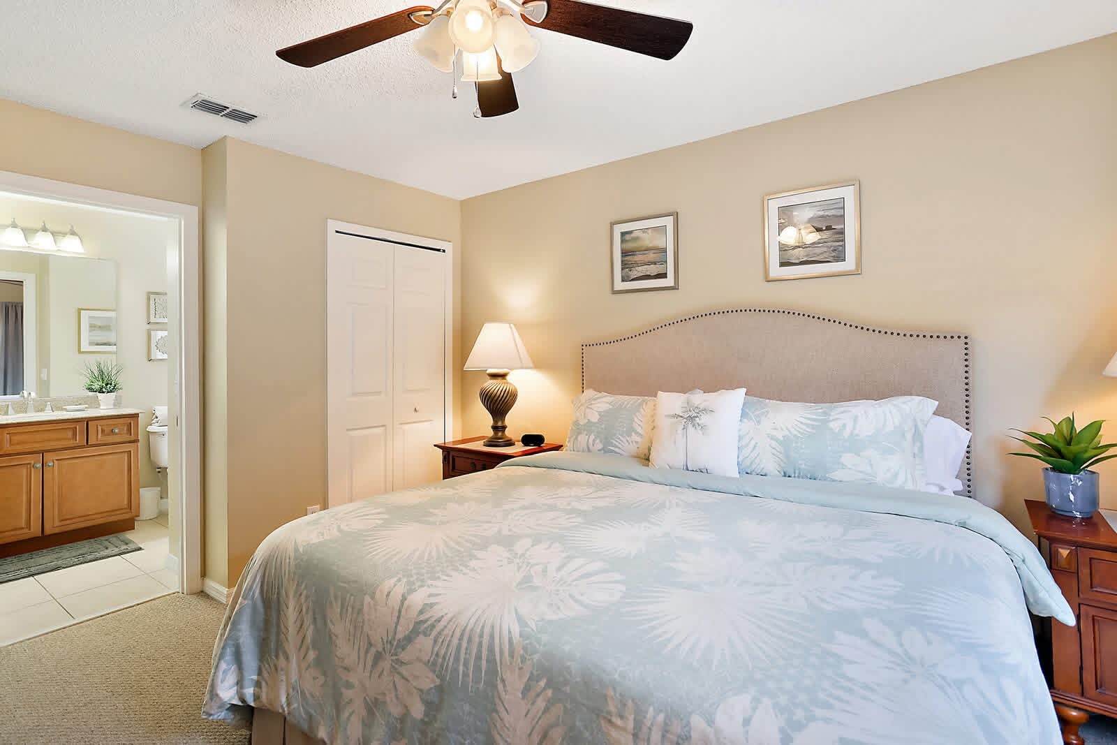 Spacious master bedroom with beige walls, upholstered headboard, and en-suite bathroom visible through open door