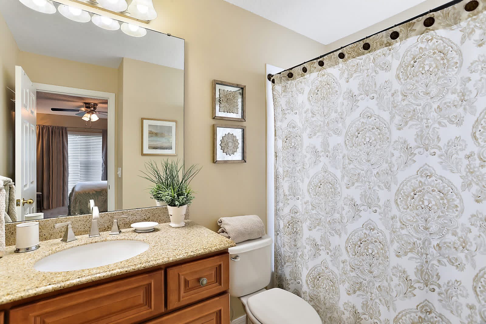 Elegant bathroom with granite countertop, wood vanity, mirror, and ornate damask shower curtain