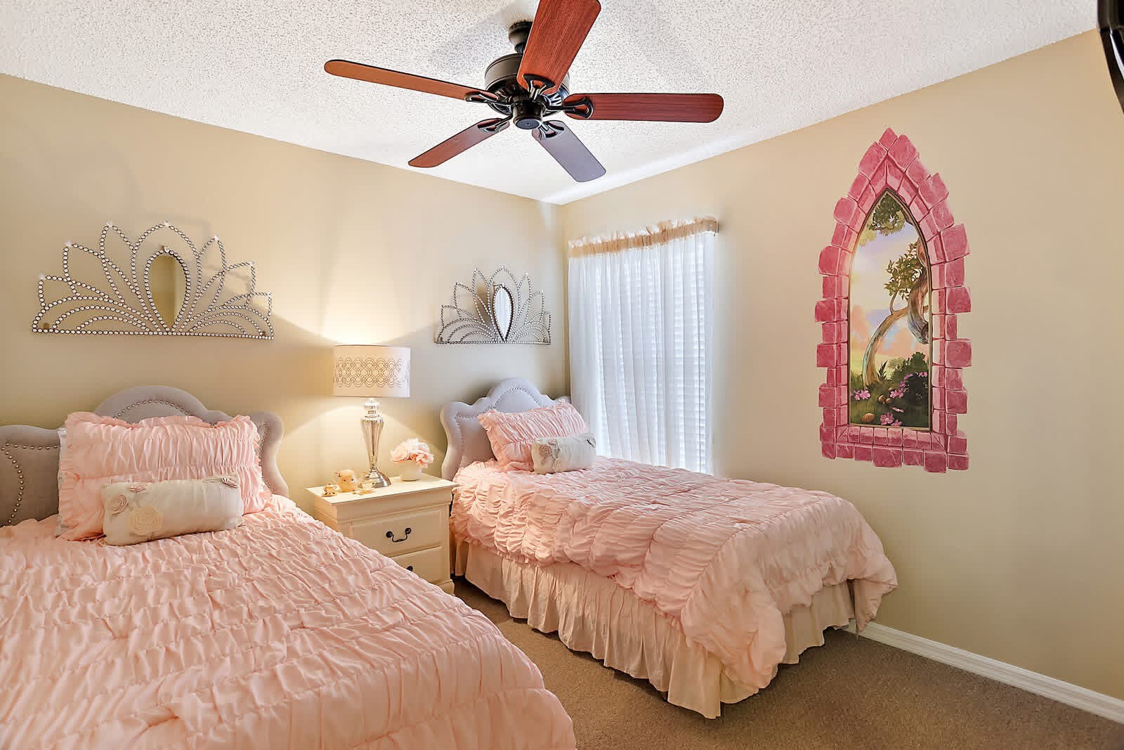 Elegant girls bedroom with two twin beds, pink bedding, decorative wall art, and ornate pink mirror frame