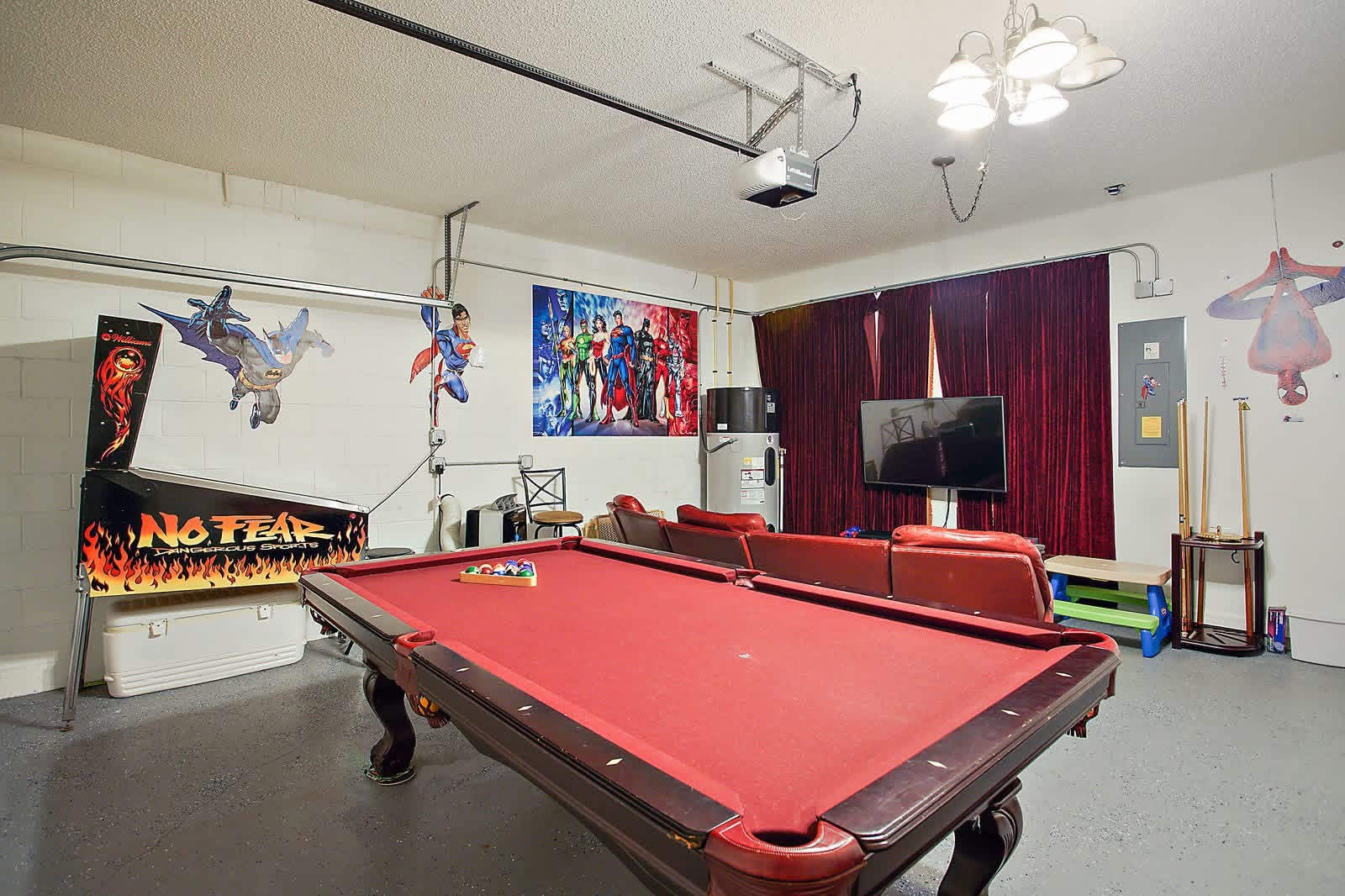 Recreation room with red pool table, arcade machine, red sofa, TV, and superhero decorations